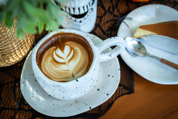 Close up of Hot coffee latte with latte art milk foam in cup mug and Homemade burnt cheesecake with decor in a coffee a theme of halloween on wood desk Halloween holiday background.