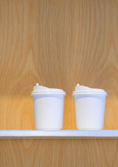 Two white double wall paper hot coffee cup mockup with plastic lid on wooden shelf in vertical frame, close up with copy space