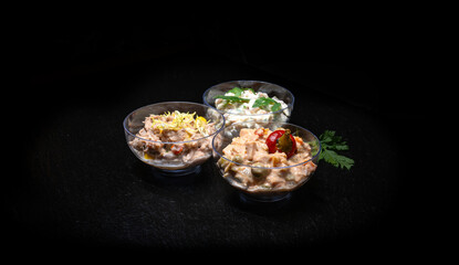 Different types of salads in a glass bowl on a black background.