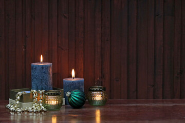 Weihnachtshintergrund: Kerzen mit Weihnachtsschmuck vor einer Holzwand.