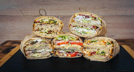Sandwiches with salad, salami, cheese and dressing on wooden table.