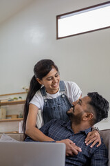 Happy Indian young couple using playing laptop computer notebook on sofa home house