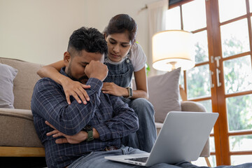 Indian couple sitting together indoors in the home house, calculating finances at home, looking...