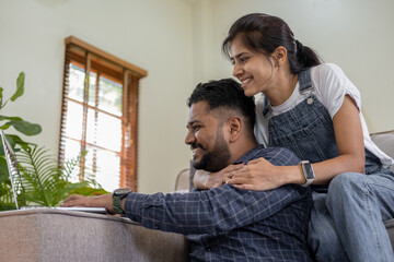 Happy Indian young couple using playing laptop computer notebook on sofa home house