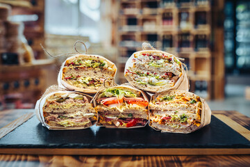 Sandwiches with salad, salami, cheese and dressing on wooden table in restaurant.
