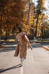 A beautiful adult woman in a coat and hat walks on the road in the middle of the city in the autumn season