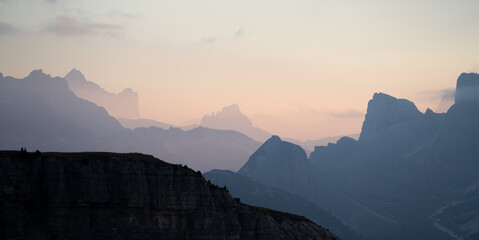Colourful sunset over sharp rocky mountain ranges layering in the distance , Dolomites, Italy