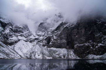 Breathtaking panorama of the "Czarny Staw" lake in winter, surrounded by snow-covered rocky mountains that pierce through a veil of mist, reflecting the stillness and depth of nature.