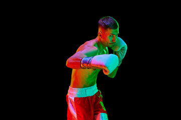 Young sportsman, professional boxer, mixed martial art fighter training against over black mode background in mixed neon filter, light.