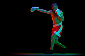 Fototapeta na wymiar Professional male boxer, mixed martial art fighter training against black mode background in mixed neon filter, light.