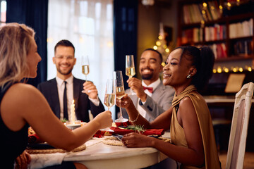Happy black woman and her friends toasting with champagne during Christmas dinner party.