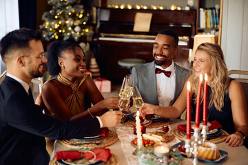 Group of happy friends toasting with champagne while celebrating during Christmas dinner at dining table.