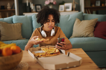 Teenage boy using phone while having pizza at home