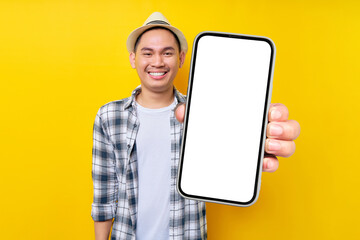 Satisfied handsome Asian young man 20s wearing casual clothes hat looking camera, Showing mobile cell phone with blank screen workspace area isolated on yellow background. People lifestyle concept - Powered by Adobe