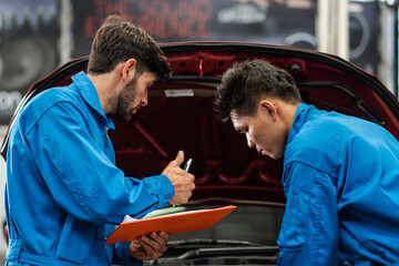 Auto mechanic checking maintenance checklist while colleague worker repair car at auto garage shop. After service for safety vehicle