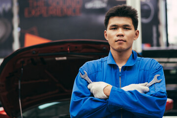 Asian male automotive mechanic man holding wrench in arms crossed in auto garage, transport business and after service concept