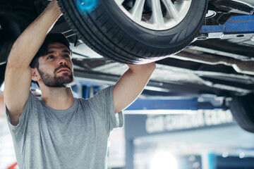 Caucasian car mechanic replace tyre on wheel at auto garage shop. Technician worker checking after...