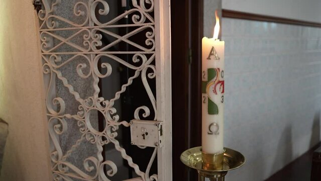 Decorated Paschal candle burning beside ornate metal grille inside church