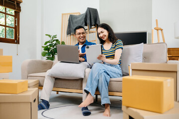 Asian young attractive couple man and woman use tablet and smartphone online shopping furniture decorate house with carton package move in new house. Young married moving home. .