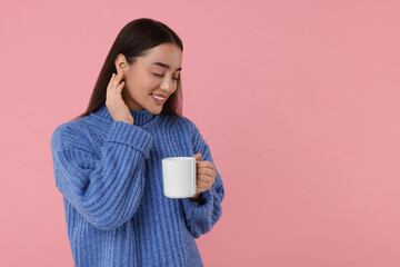 Happy young woman holding white ceramic mug on pink background, space for text