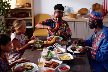 African American family of four in ethnic apparel sitting by festive table served with national...