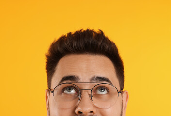 Man in glasses looking up on orange background, closeup