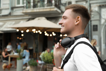 Smiling man with headphones walking outdoors. Space for text