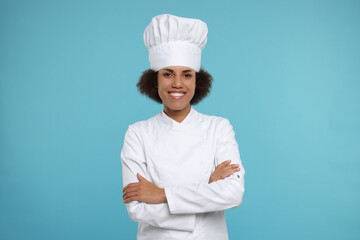 Portrait of happy female chef in uniform on light blue background