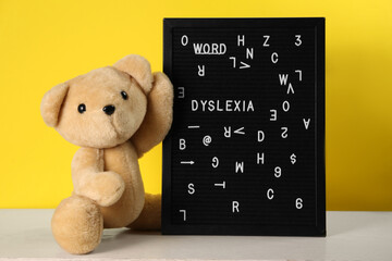 Black letter board with word Dyslexia and teddy bear on light table against yellow background - obrazy, fototapety, plakaty