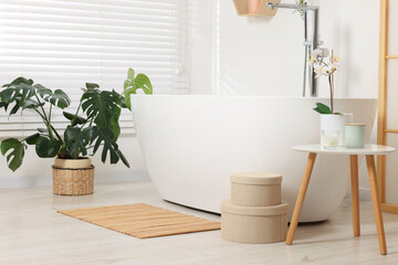 Stylish bathroom interior with bath tub, houseplants and bamboo mat