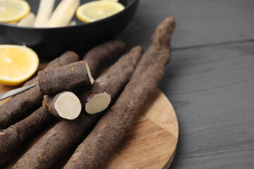 Raw salsify roots with lemon on grey wooden table, space for text