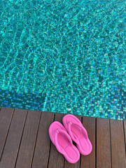 Naklejka premium Clear rippled water in swimming pool and pink flip-flops on wooden deck outdoors, above view. Space for text