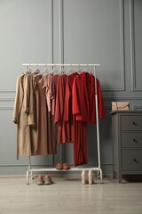 Rack with different stylish women`s clothes, shoes and bag on chest of drawers near grey wall...