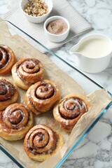 Tasty cinnamon rolls in baking dish served on white marble table, above view