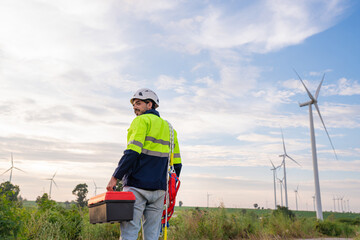 Engineer wearing uniform hold equipment box inspection work in wind turbine farms rotation to generate electricity energy. Maintenance engineer working in wind turbine farm at sunset.