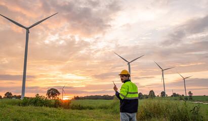 Engineer wearing uniform inspection and survey work in wind turbine farms rotation to generate electricity energy. Maintenance engineer working in wind turbine farm at sunset.