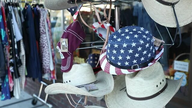 Variety of cowboy hats and American themed hats on a rack outside of a thrift store.