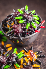 Scary sweet jelly spiders. Halloween candies in bowl on black table.