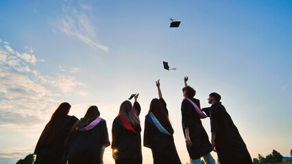 Student graduates toss their caps at sunset.