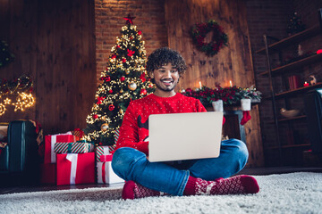 Full length photo of arab guy sitting carpet floor using netbook browsing internet website shop isolated on xmas decorated home background
