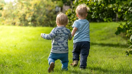 Fotobehang Zwei Kleinkinder laufen voller Freude über eine Wiese © DZiegler