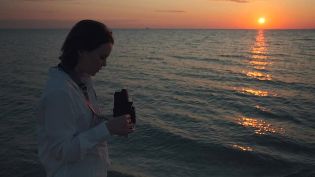 Young woman holding tlr retro vintage medium format 120 mm film camera making photographs of the sea. Female photographer taking photos on beach on sunset