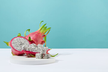 Fresh dragon fruit is displayed on a round white podium with a blue-white background. Space for...