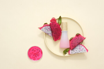 Pink bottle with wooden lid without label and fresh dragon fruit displayed on ceramic plate and petri dish containing red dragon fruit extract. Dragon fruit contains a lot of fiber and no fat.