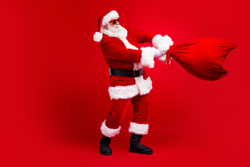 Fototapeta na wymiar Full length photo of cheerful cool man fairy character santa claus carrying new year gifts north pole advent isolated on red color background