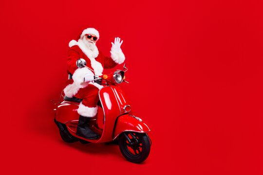 Full size photo of funky grandfather wear stylish santa costume glasses riding on red scooter say hello isolated on red color background