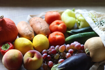 Reusable mesh bag with seasonal fruit and vegetable on wooden background. Late summer or early autumn. Selective focus.