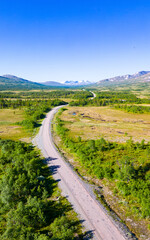 Fototapeta na wymiar Typical scandinavian landscape with a road leading through forests and wetland with mountains in the background