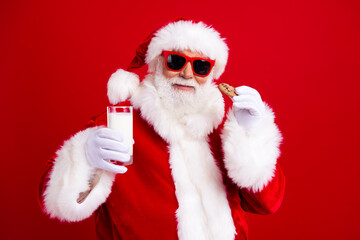 Photo of pleasant grandfather wear stylish santa costume hold glass of milk cookies at christmas eve isolated on red color background