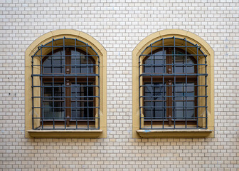 Two arched wooden windows protected by metal grilles. Set in a stone window band and white brick wall
